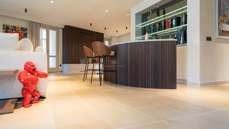 Bar contemporain avec boiseries rainurées, tabourets en cuir et sol en pierre dans une villa de luxe.