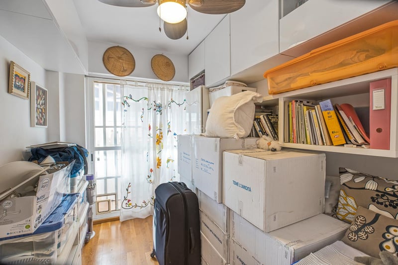 Ein kleiner Raum mit weißen Einbauschränken, Regalen, Umzugskartons, einem Deckenventilator und natürlichem Licht.