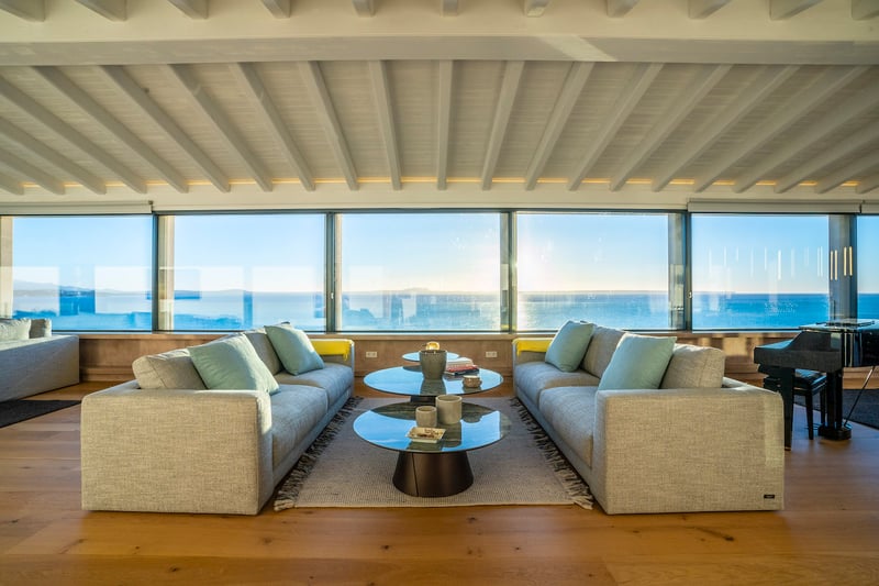 Modernes Wohnzimmer mit grauen Sofas, Glastischen und bodentiefen Fenstern mit Blick auf das Mittelmeer.