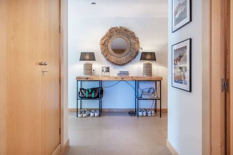 Couloir avec console en bois brut, miroir soleil en fibres et lampes en corde sur sol clair.