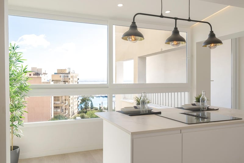 Weiße Kücheninsel mit Induktionskochfeld vor einem großen Fenster mit Blick auf den Hafen und die Stadt.