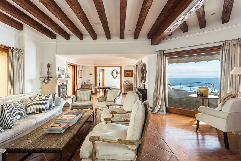 Grand balcon avec vue sur mer depuis un appartement moderne. Garde-corps en verre, plancher en bois et mobilier extérieur élégant.