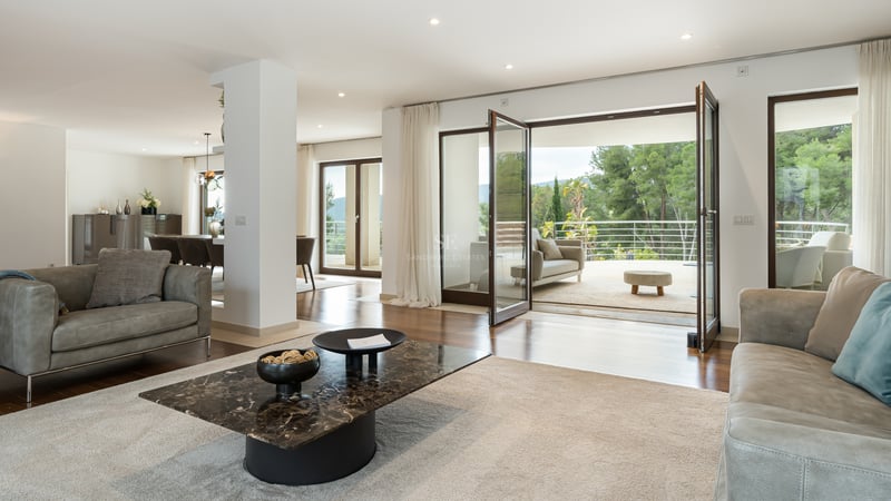 Salon moderne avec canapés en cuir, table en marbre et grandes baies vitrées ouvrant sur une terrasse vue forêt.