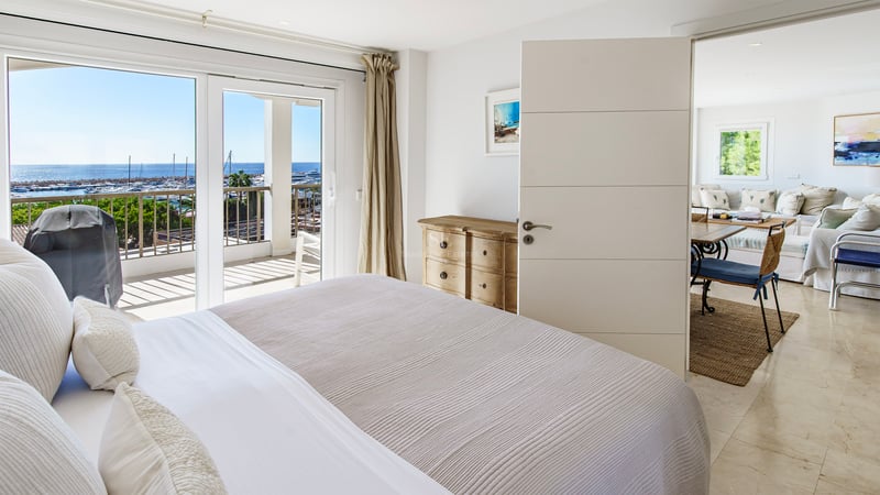 Bright bedroom featuring a large bed, sliding doors to a terrace, and panoramic views of a marina.