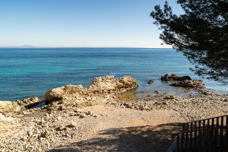 Erhöhte Aussicht auf eine felsige Mittelmeerbucht mit klarem türkisfarbenem Wasser und weitem Horizont.