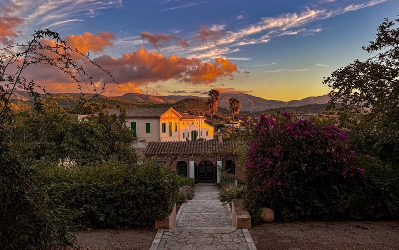 Naturskön utsikt över en vit medelhavsvilla med terrakottatak vid solnedgången, omgiven av prunkande trädgårdar och berg.