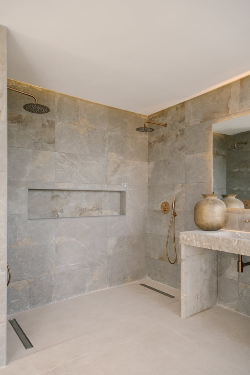 Luxuriöse begehbare Dusche mit großformatigen Natursteinfliesen, Doppel-Regenduschköpfen aus Bronze und Steinwaschtisch.