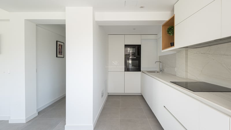 Cuisine blanche minimaliste, plans de travail effet marbre, carrelage gris et four Bosch encastré.