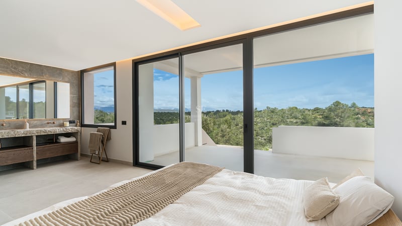 Hauptschlafzimmer mit großen Glasschiebetüren, die auf eine private Terrasse mit Blick auf grüne Hügel führen.