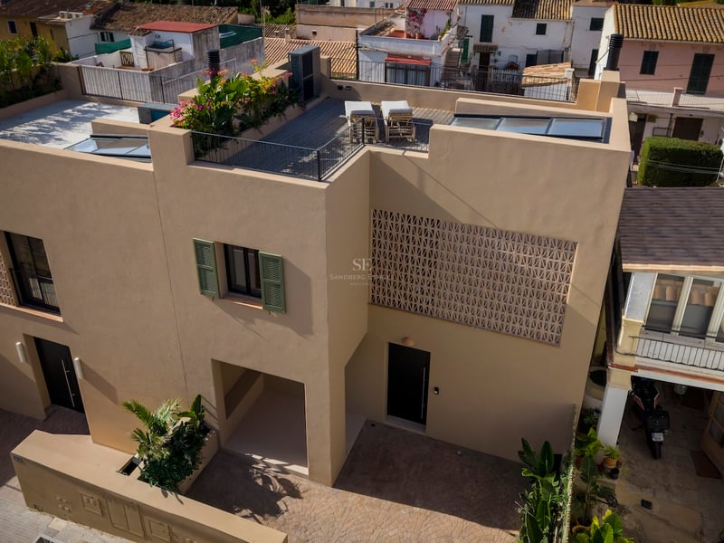 Aerial view of a modern ochre villa featuring a rooftop terrace, green shutters, and decorative lattice stonework.