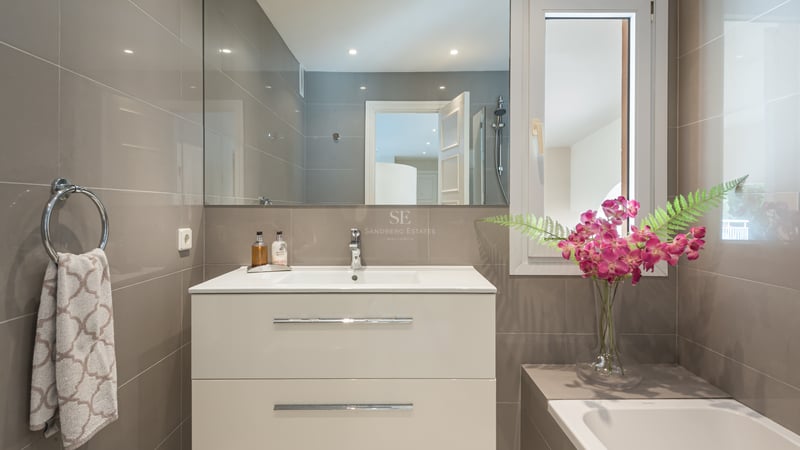 Contemporary bathroom featuring a white vanity, integrated sink, large mirror, and taupe wall tiles with chrome accents.