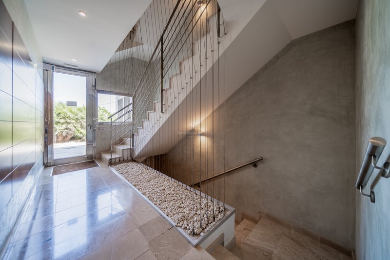 Entrée lumineuse avec sol en pierre polie, escalier à câbles et porte vitrée donnant sur le jardin.