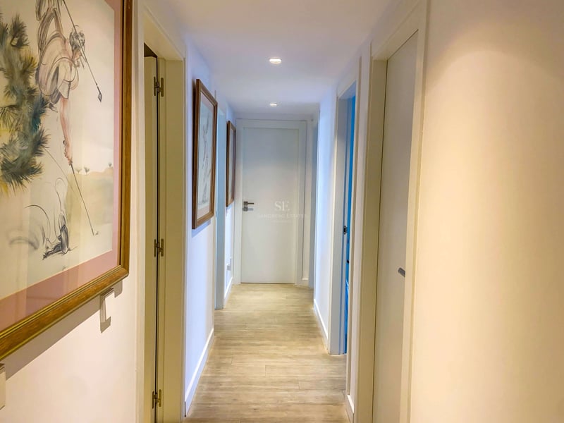 Heller Flur mit hellen Keramikfliesen in Holzoptik, weißen Türen und gerahmten Golf-Kunstwerken.