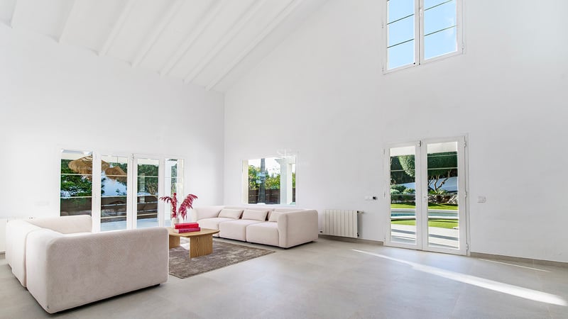 Rymligt vardagsrum med vita ryggåstak, beige soffor och altandörrar som leder ut till trädgården.