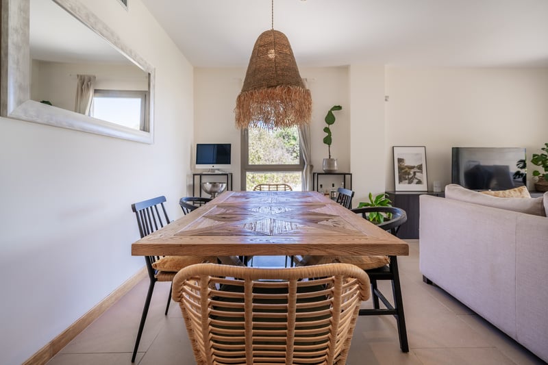Grande table à manger en marqueterie de bois avec suspension en rotin dans un salon moderne et lumineux.