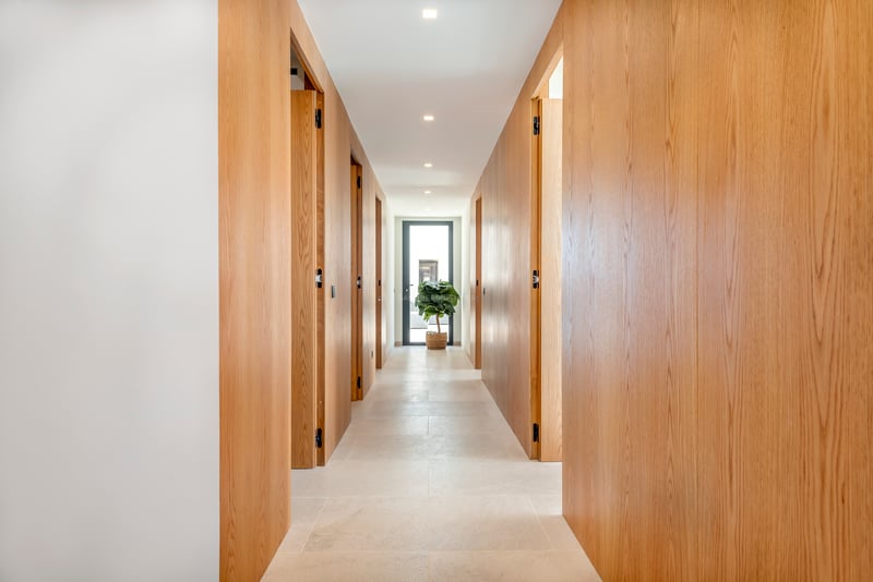 Couloir moderne lumineux avec des panneaux en bois de chêne du sol au plafond et des portes affleurantes.