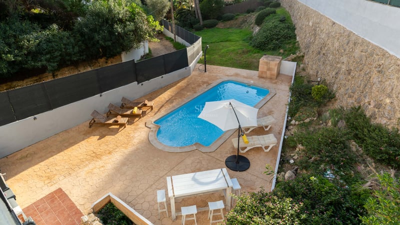 Vue aérienne d'une piscine turquoise entourée d'une terrasse en terre cuite avec transats et coin repas.