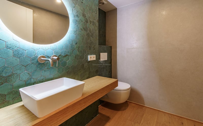 Salle de bain moderne avec carreaux hexagonaux vert canard, vasque à poser sur bois et miroir rétroéclairé.