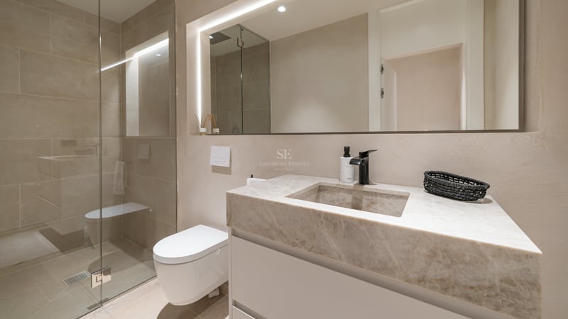 Salle de bains moderne avec vasque en marbre, miroir rétroéclairé, WC suspendu et douche à l'italienne en verre.