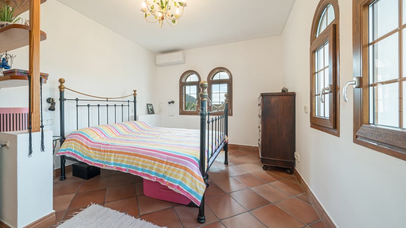 Bright bedroom featuring terracotta tile flooring, a wrought iron bed frame, and traditional arched wooden windows.