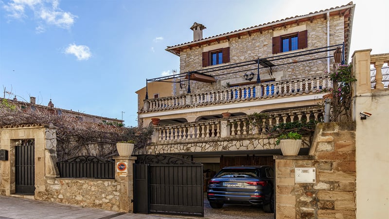 Three-story traditional stone house with terracotta roof, multiple balustraded terraces, and an integrated garage entrance.
