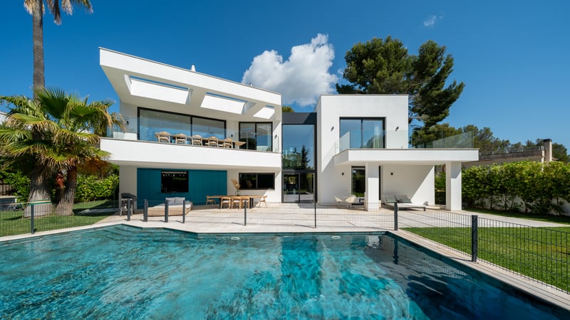 Extérieur d'une villa blanche moderne avec grande piscine, balustrades en verre et palmiers.