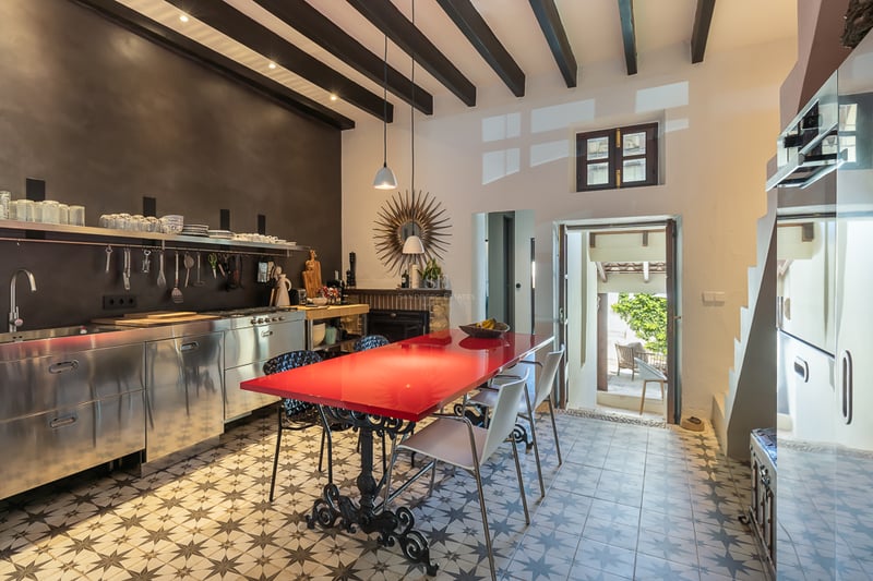 Cuisine moderne avec placards en inox, table rouge et carrelage hydraulique traditionnel.