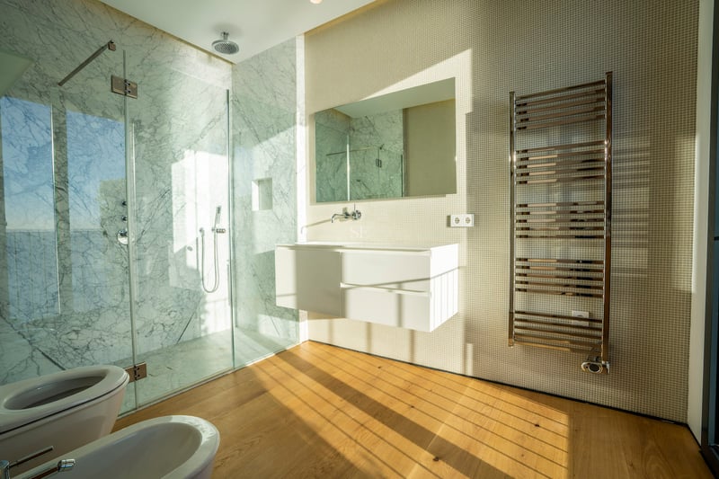 Modernes Badezimmer mit bodengleicher Marmordusche, schwebendem Waschtisch und Eichenparkett im Sonnenlicht.