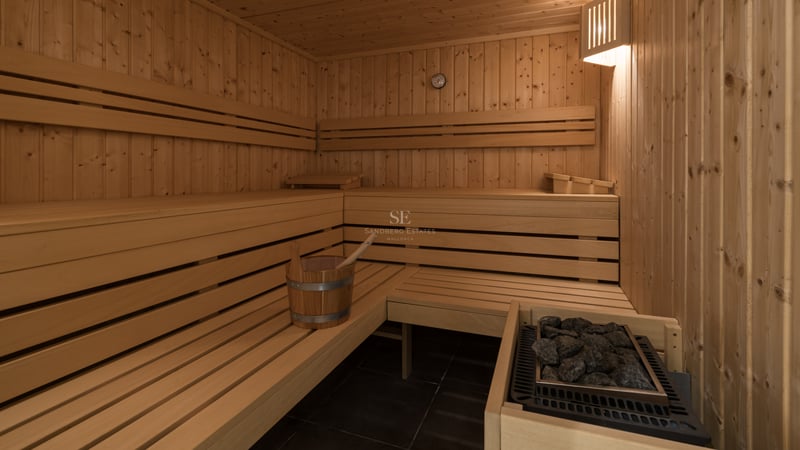 Vue intérieure d'un sauna en bois avec bancs à plusieurs niveaux, poêle à pierres et seau en bois.