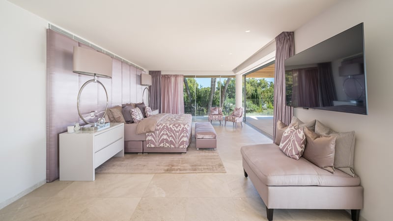 Luxuriöses Schlafzimmer mit Kingsize-Bett und Glasfronten zum grünen Garten.