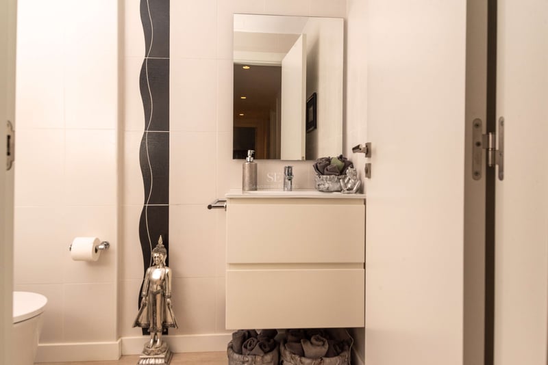 Cremefarbenes Badezimmer mit weißem Waschtisch, rechteckigem Spiegel und silberner Buddha-Statue.