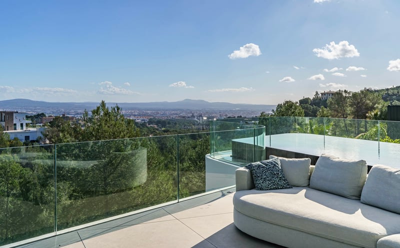 Terrasse moderne avec canapé design, garde-corps en verre et piscine surplombant la ville et les montagnes.