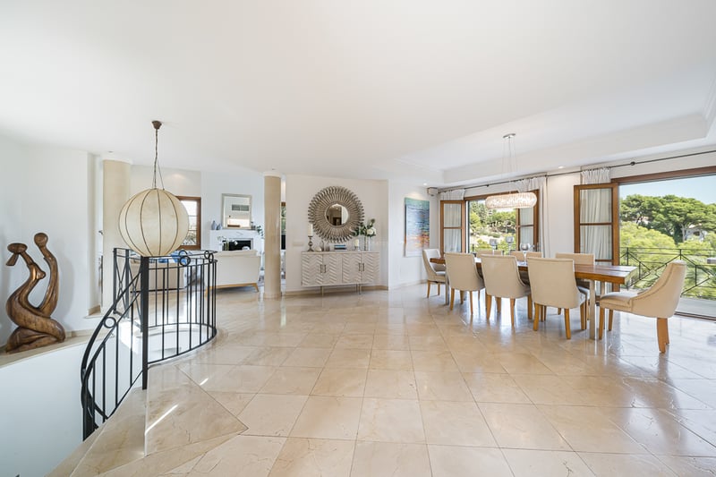 Rymlig matsal med beige marmorgolv, träbord och naturligt ljusinsläpp från stora dörrar.