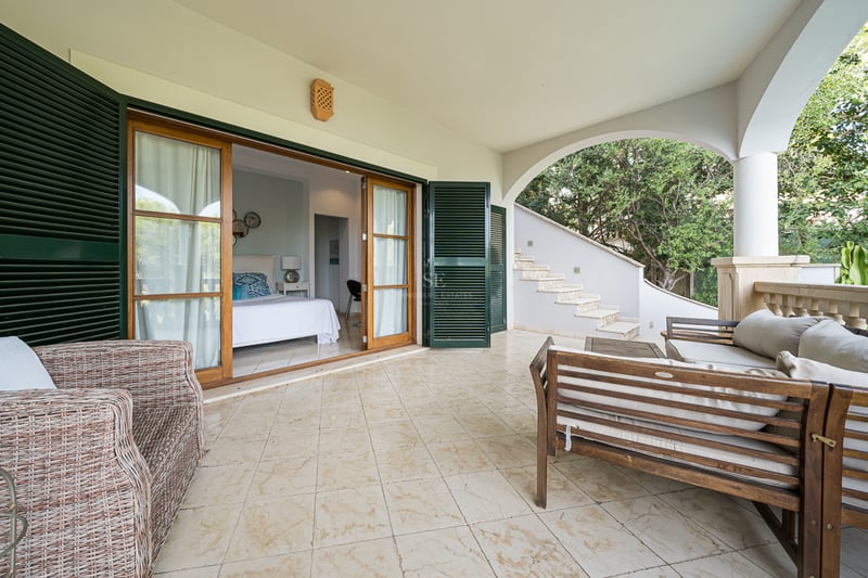 Övertäckt medelhavsterrass med klinkergolv, trämöbler och stora skjutdörrar som leder till ett sovrum.