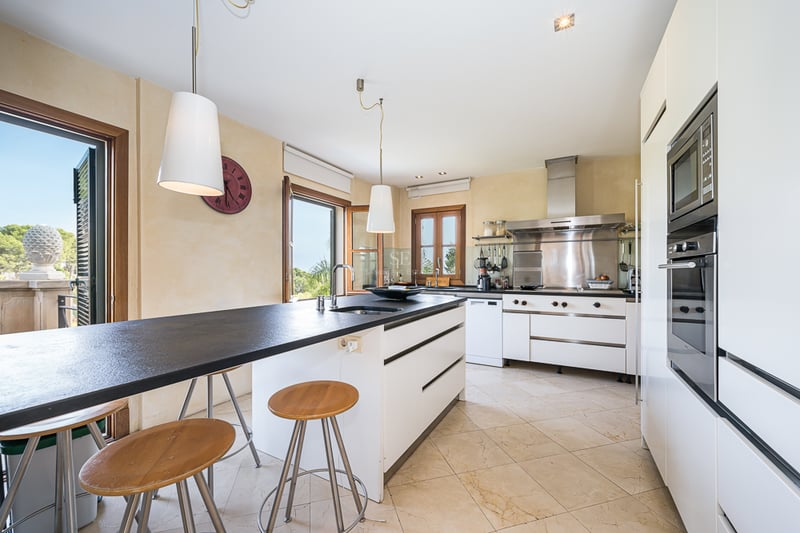 Modernt kök med mörk köksö, barstolar i trä, mörk bänkskiva och vitvaror i rostfritt stål.