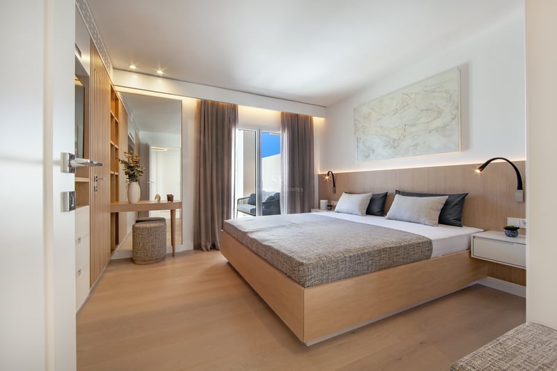 Chambre de maître moderne avec lit en bois, éclairage intégré et accès à un balcon ensoleillé.