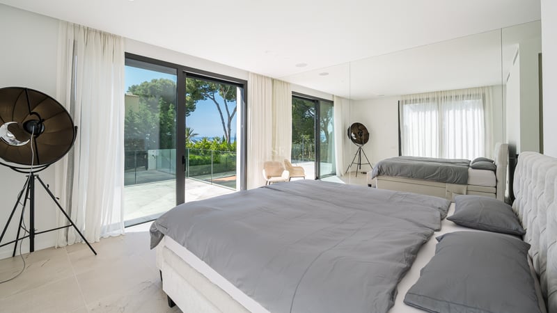 Chambre moderne avec grand lit, baies vitrées et terrasse privée offrant une vue sur les pins et la mer.