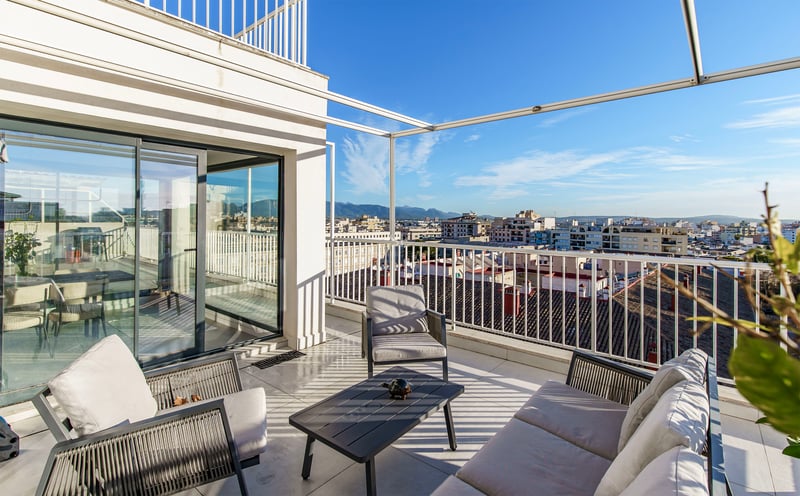 Grande terrasse blanche avec canapé et fauteuils d'extérieur modernes surplombant la ville et les montagnes.