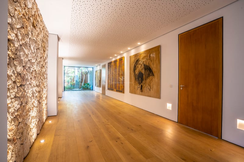 Langer moderner Flur mit Eichendielen, weißen Wänden mit Kunstwerken und Glastür zum Garten am Ende.