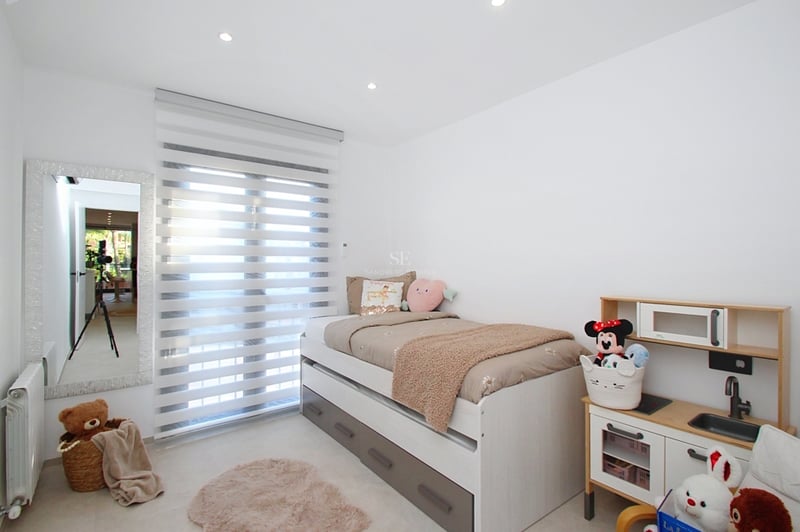 Vitt sovrum med säng med förvaring, helkroppsspegel, zebrapersienner och leksakskök.