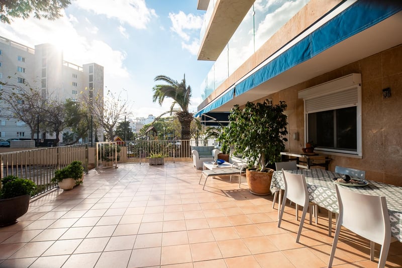 Große Außenterrasse mit Terrakottafliesen, Esstisch, Loungemöbeln und blauen Markisen bei strahlendem Sonnenschein.