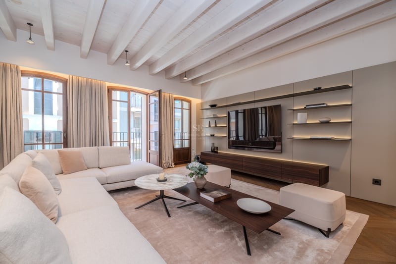 Modern luxury living room featuring exposed white beams, cream L-shaped sofa, and bespoke walnut media unit.