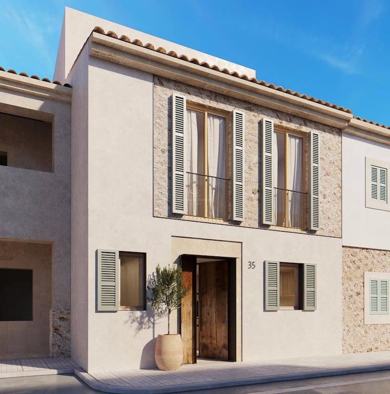 Bâtiment en stuc beige avec volets vert sauge, accents en pierre naturelle et porte en bois sous un ciel bleu.