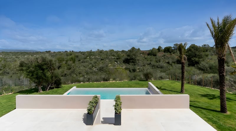 Rechteckiger Infinity-Pool mit heller Steinterrasse und Blick auf die grünen mediterranen Hügel.