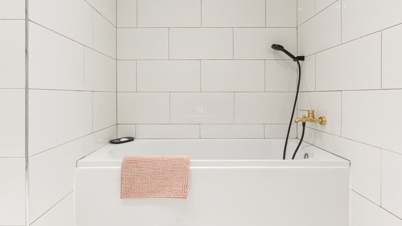 Baignoire blanche, carrelage mural, robinetterie dorée et pommeau de douche noir.