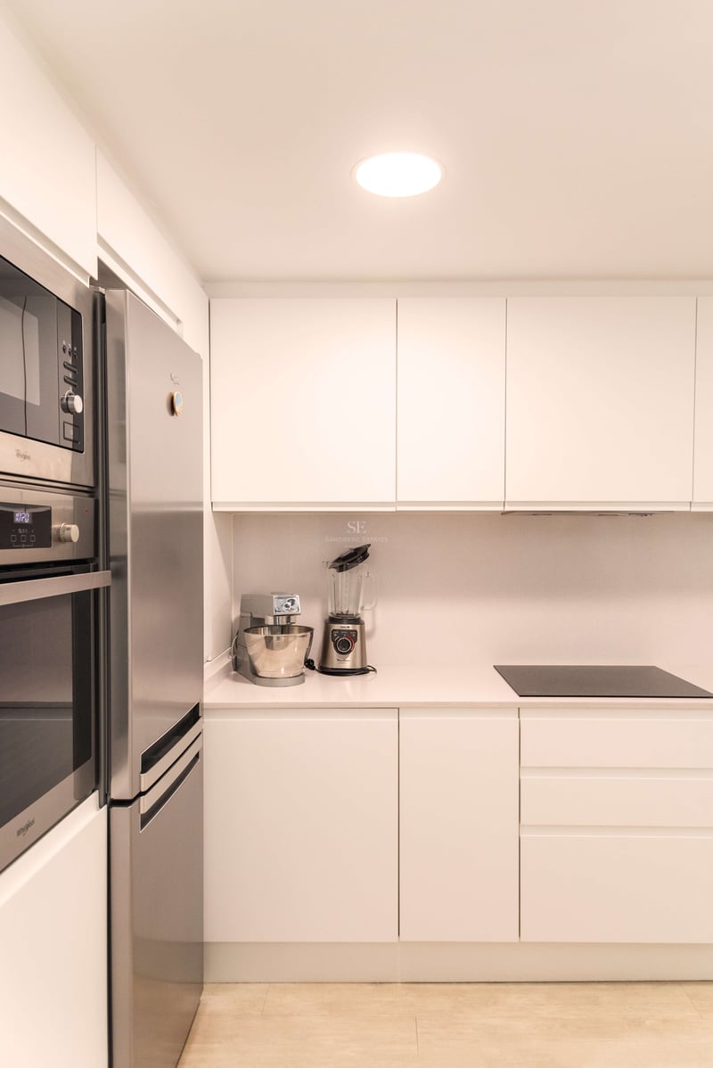 Weiße minimalistische Küche mit Edelstahlgeräten, Steinarbeitsplatte und grifflosen Schränken.
