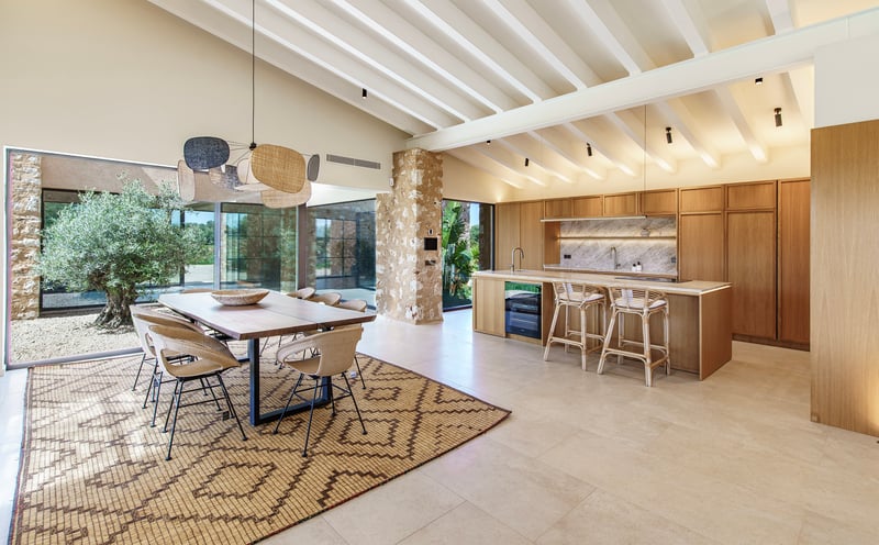 Offene Designerküche mit Holzelementen, Essplatz, weißen Deckenbalken und Natursteinwand.