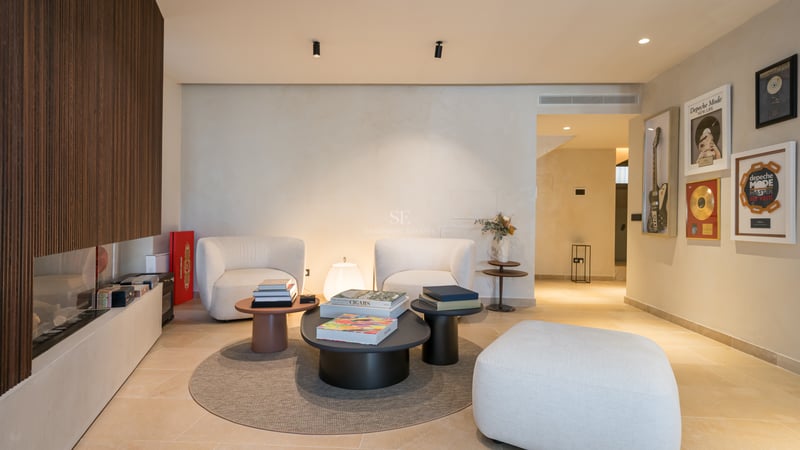 Espace lounge moderne avec fauteuils blancs, tables basses anthracite et mur en tasseaux de bois avec cheminée.