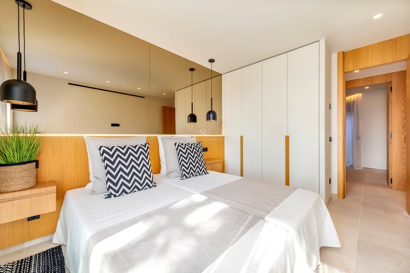 Chambre contemporaine avec tête de lit en bois, mur de miroirs et grands placards blancs intégrés.