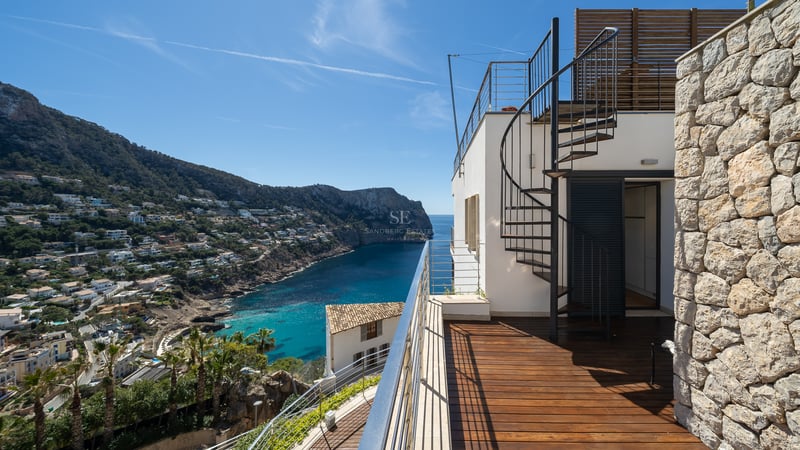 Terrace with wooden decking and a spiral staircase overlooking a Mediterranean bay and mountains.
